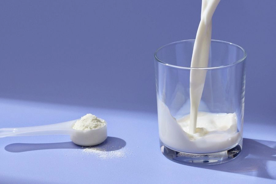 milk being poured in glass next to a spoon of powder